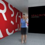 Office branding concept using enlarged white letter fragments on a red wall and the Arachnys wordmark on a black panel.